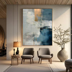 Large minimalist abstract painting with textured blue, white, and gold brushstrokes, titled 'Blue Threshold', displayed in a modern living room with gray chairs and a wooden side table.
