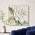 3D textured white peony wall art with green foliage, framed, above blue sofa