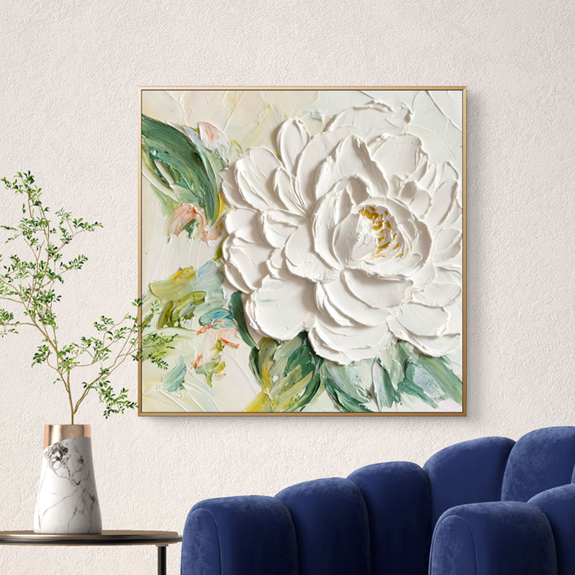 3D textured white peony wall art with green foliage, framed, above blue sofa
