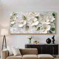 3D textured white floral wall art with gold frame, featuring soft green leaves and golden centers, displayed in a modern living room with beige sofa and console table.