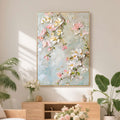 3D textured floral wall art 'Spring Reverie' with pink and white blossoms on soft light blue background, hand-painted canvas in bright living room setting.