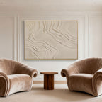 Modern living room with two beige armchairs and a wooden side table, featuring a textured wall art piece.