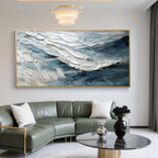 Abstract Modern Wave Wall Art – Breakwave: Hand-painted canvas with thick, textured blue, white, and gray waves in a gold frame, displayed in a modern living room with green sofa and marble coffee table.