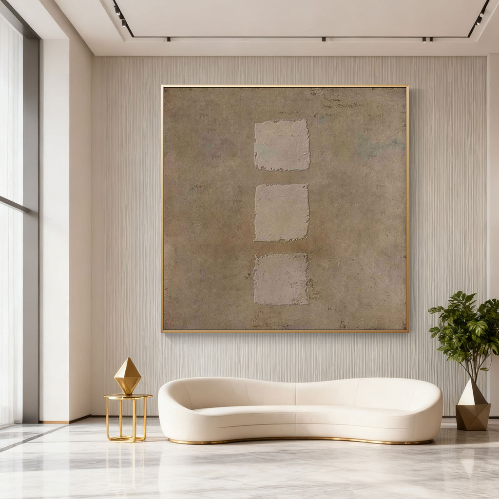 Wabi-Sabi geometric wall art featuring three textured earth-toned squares in vertical sequence, gold-framed, displayed in a modern living room with white curved sofa and gold accents.
