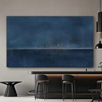 Minimalist abstract blue wall art 'Distant Night' with deep navy and indigo tones, subtle horizon line, displayed in a modern kitchen with dark bar stools and pendant lights.