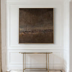 Abstract painting in a gold frame on a white wall above a gold console table.