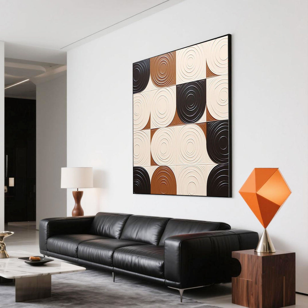 Modern abstract geometric 3D textured wall art featuring cream, brown, and black circular patterns, hand painted on square canvas, styled above a black leather sofa in a minimalist living room, museum-grade canvas, gallery-level packaging, eco-friendly materials.