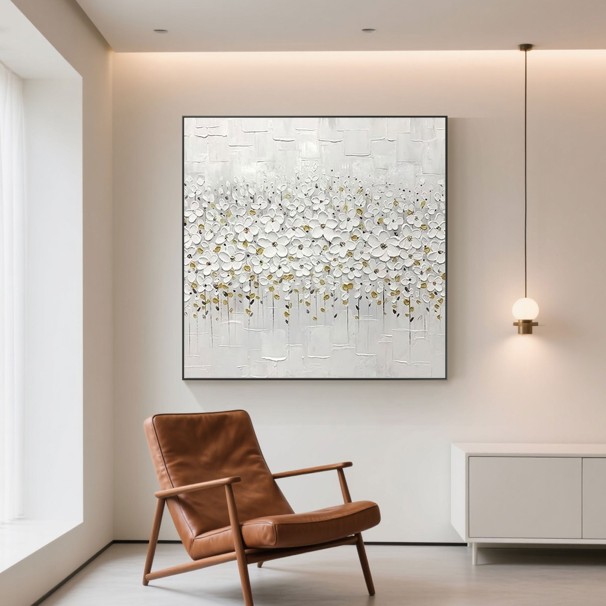 White bloom floral wall art hanging above a cabinet, next to a brown leather chair.