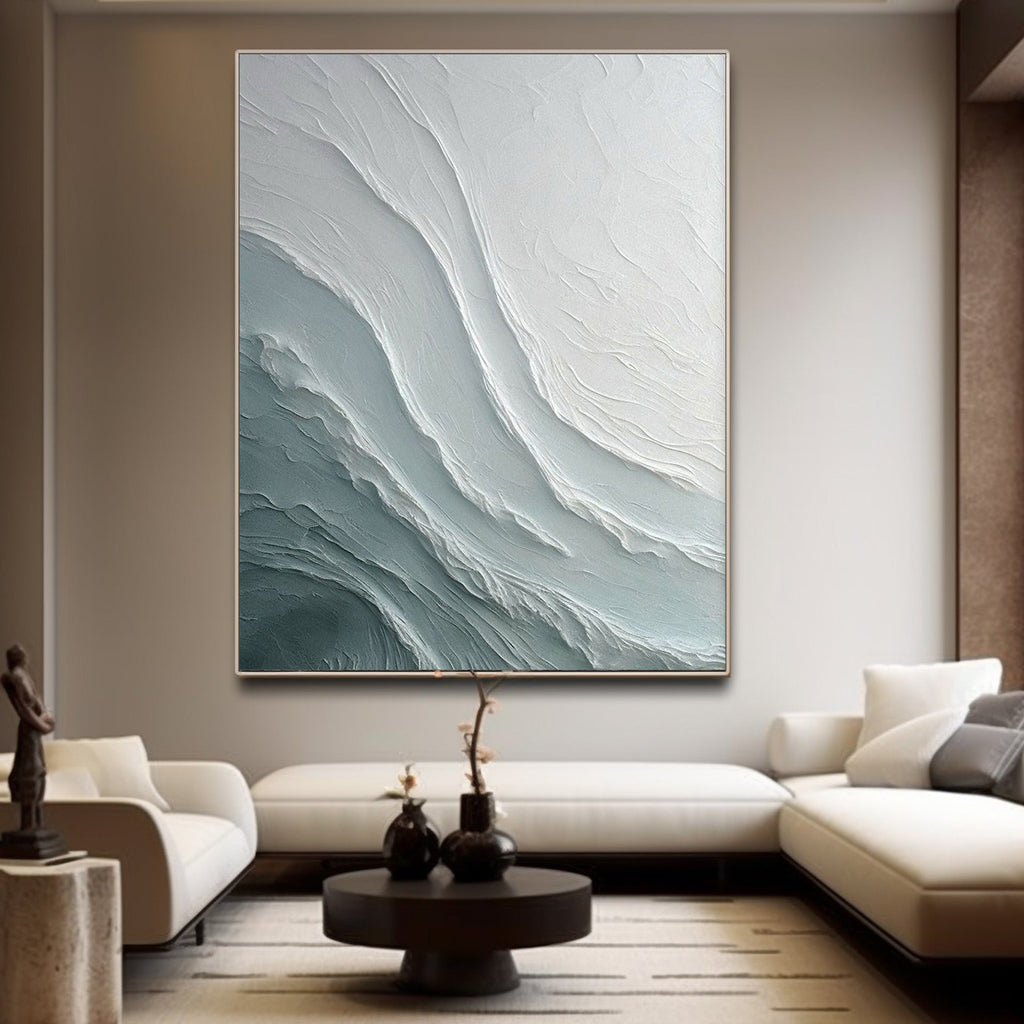 An artistic painting with undulating textures resembling water - waves adorns a white wall in a minimalist living room. Below it, a stylish light - colored sofa and an exquisite coffee table create a serene and elegant home atmosphere.