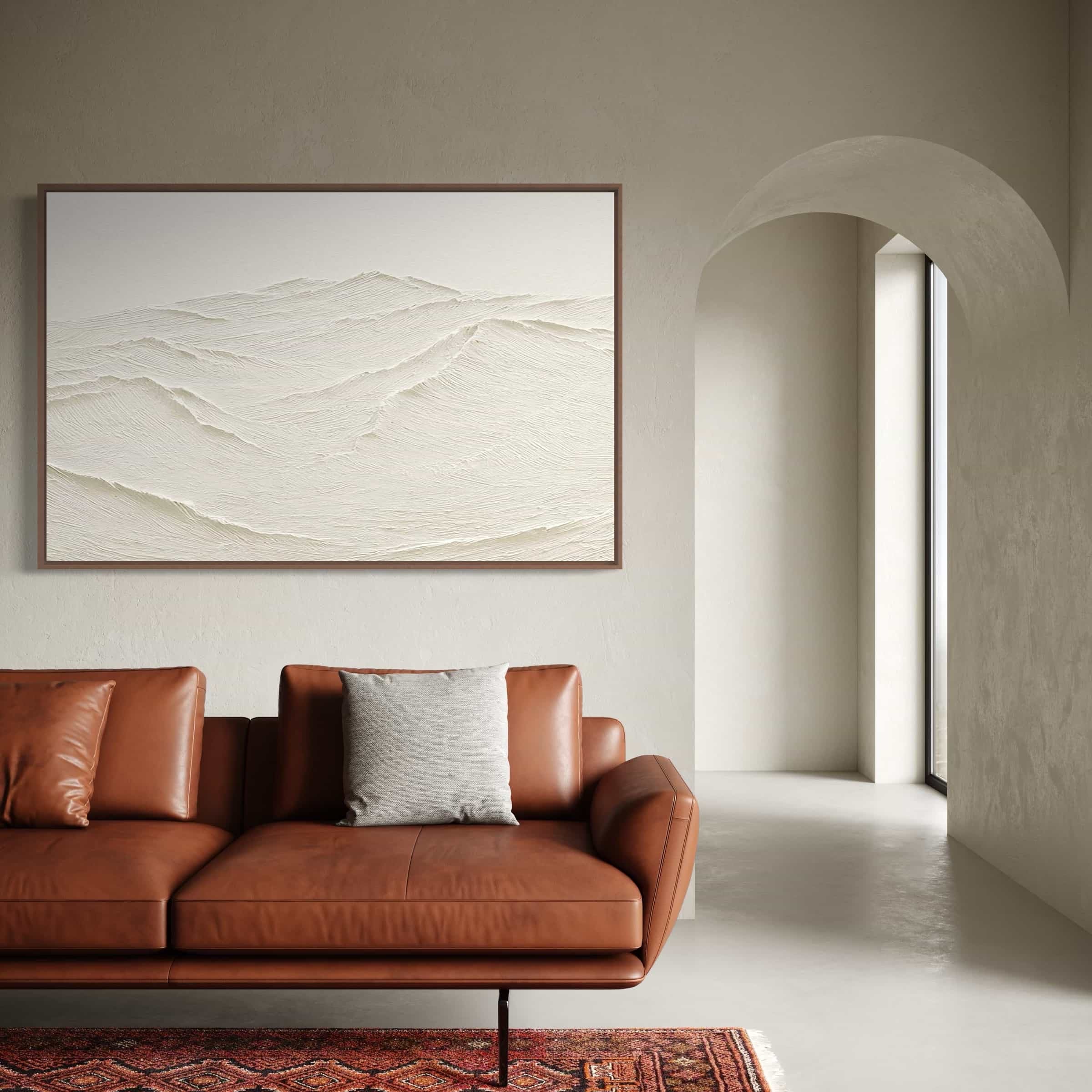 Close-up of textured painting showing layered brushstrokes in cream and white, hung above mid-century modern leather sofa with throw pillows