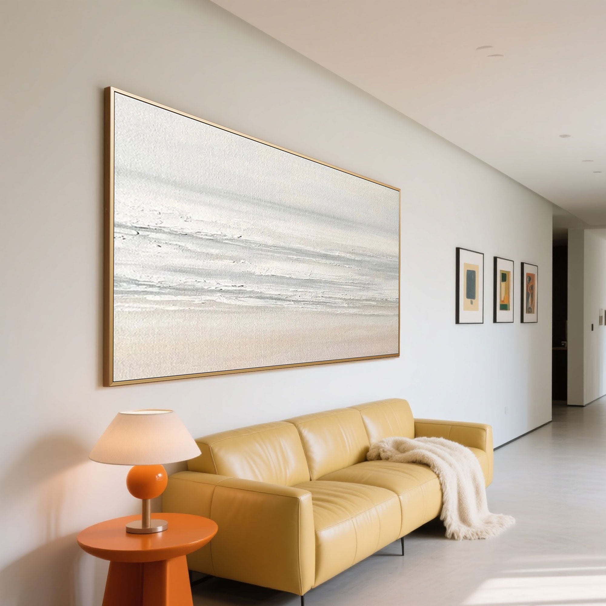 Minimalist abstract seascape art with golden frame hanging on the wall above yellow sofa.
