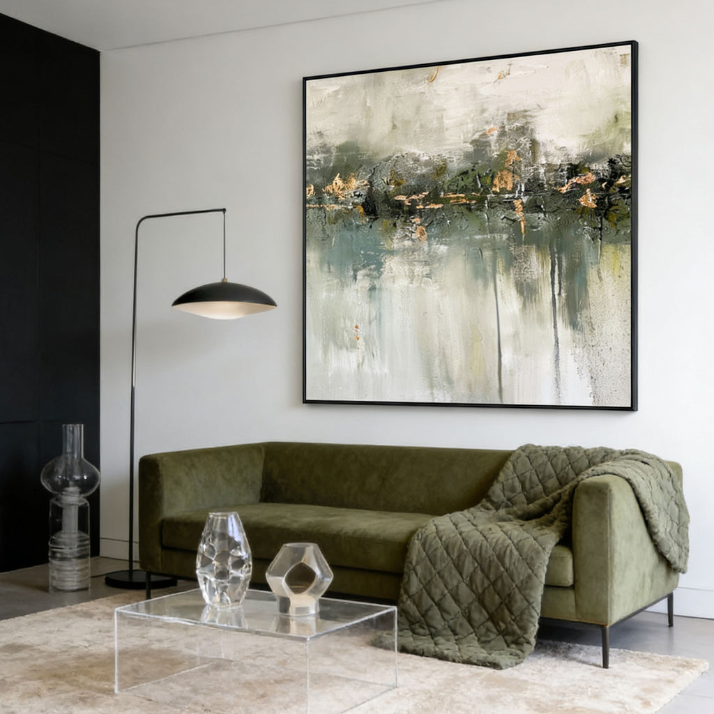 Minimalist wabi-sabi green abstract painting 'Silent Verdure' with white and gold accents, black frame, displayed in a modern living room with olive green sofa and clear acrylic coffee table.