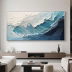 Hand-painted ocean wave art in a modern living room with a silver frame and blue and white tones.