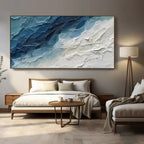 Blue and white abstract ocean canvas art displayed above a king bed.