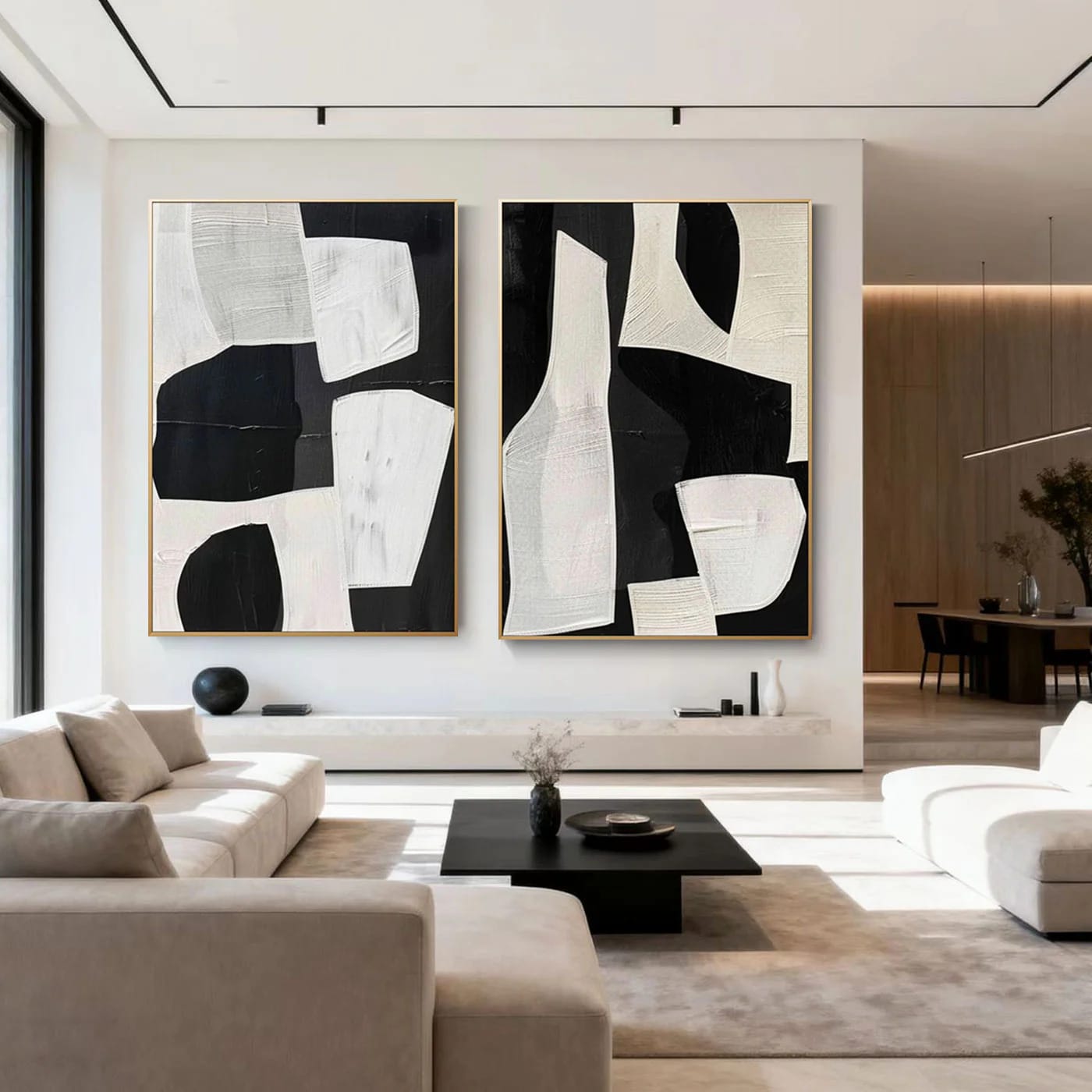 Two large modern geometric abstract paintings with black and white textured details, gold frames, displayed in a contemporary living room with neutral sofas and a black coffee table.