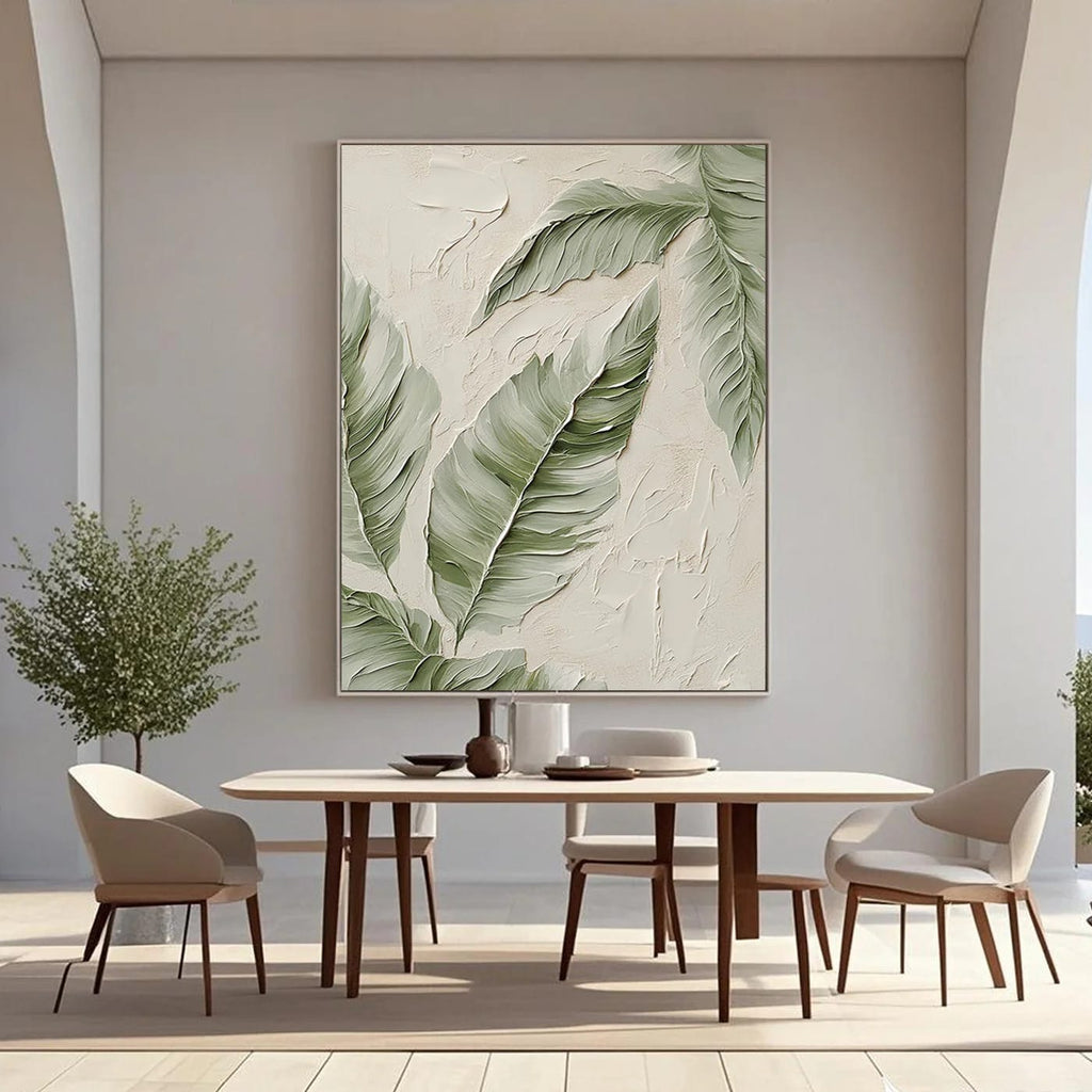 Modern minimalist hand-painted canvas with textured banana leaves in soft green on beige background, displayed in a bright dining room with neutral furniture.