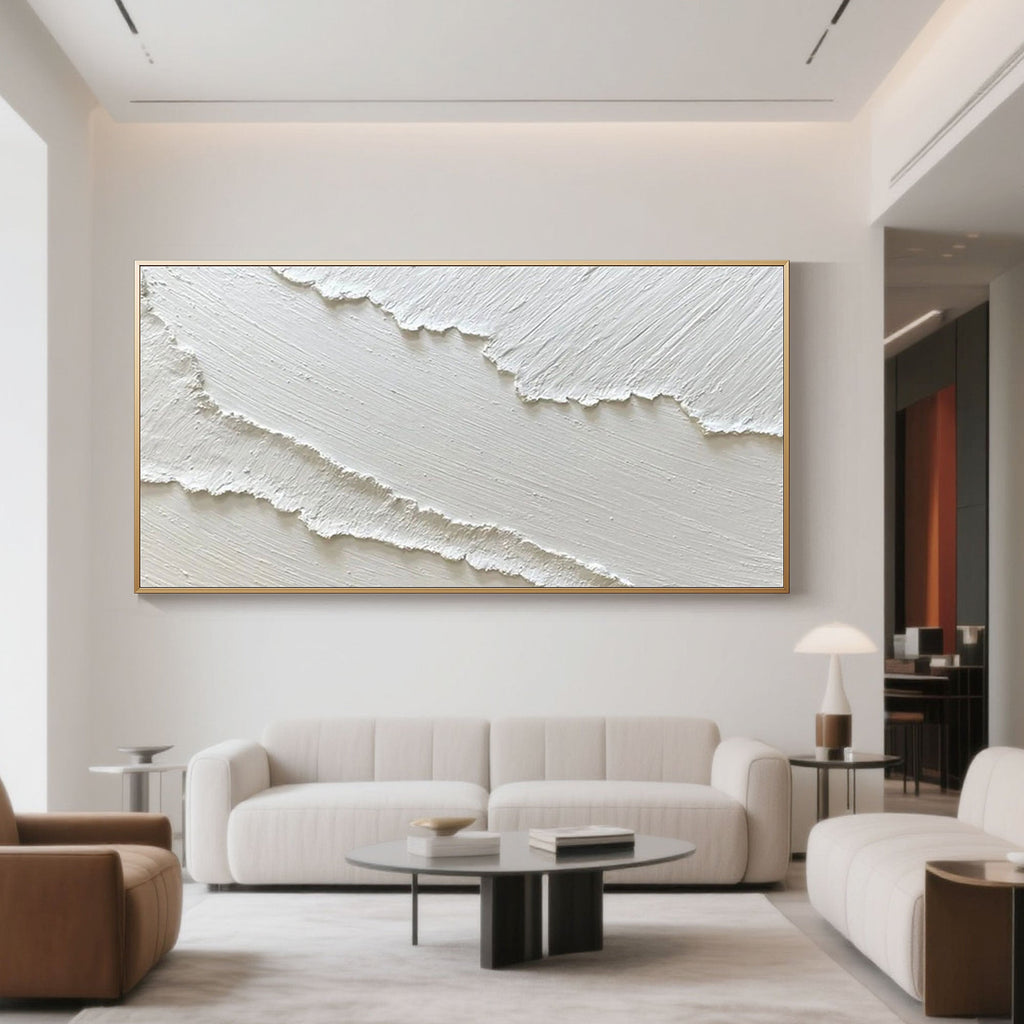 Textured white abstract ocean art with gold frame in living room setting.