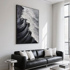 Black and white ocean painting displayed above a black leather sofa.