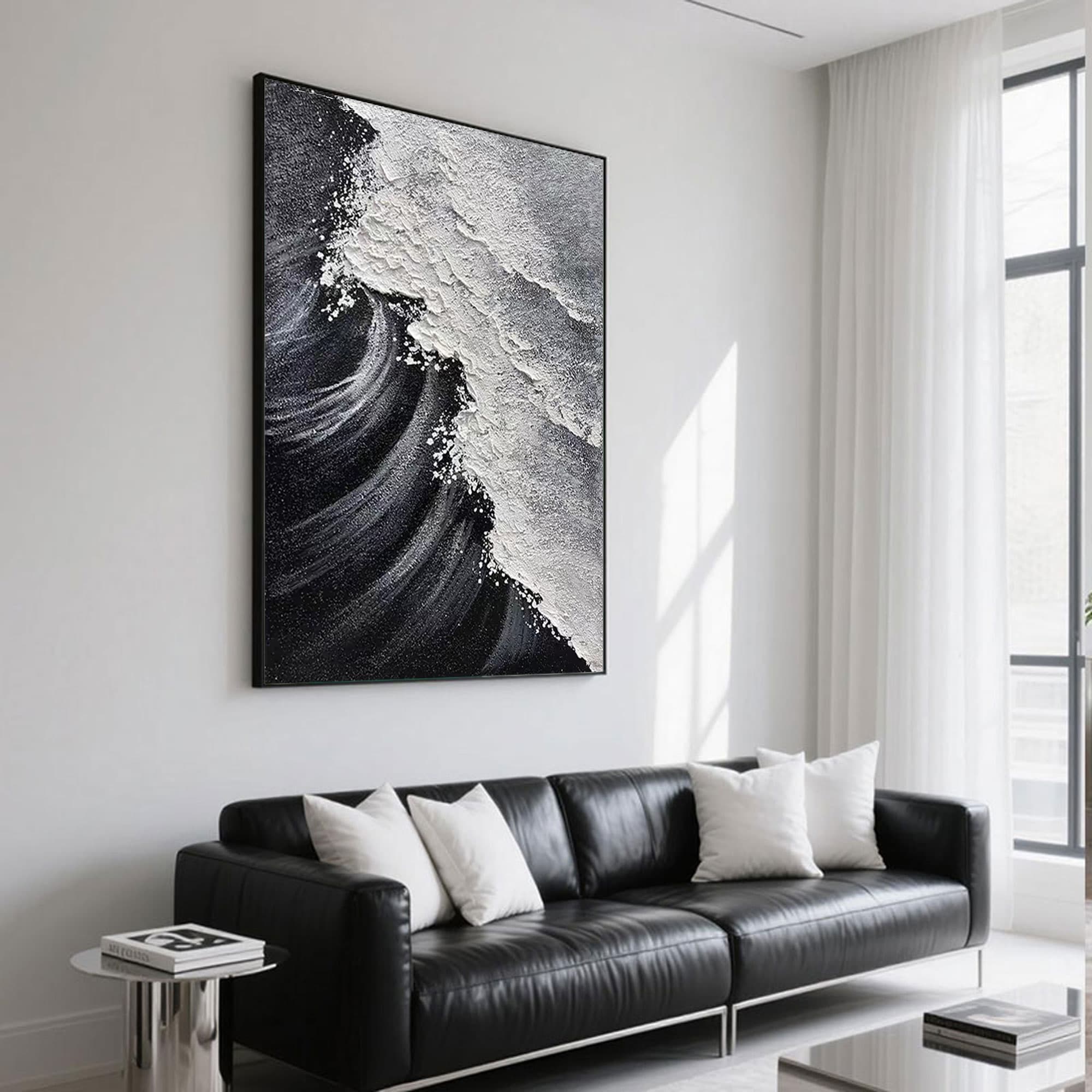 Black and white ocean painting displayed above a black leather sofa.