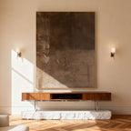 Minimalist Wabi-Sabi brown abstract painting with textured earthy layers and gold frame, mounted on beige wall above wooden console with stone base in contemporary living room.