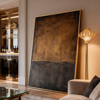 Minimalist Wabi-Sabi 'Sands of Silence' hand-painted brown and dark gray abstract wall art with textured surface and gold frame, large size, displayed in contemporary living room with sofa, floor lamp, and glass coffee table.