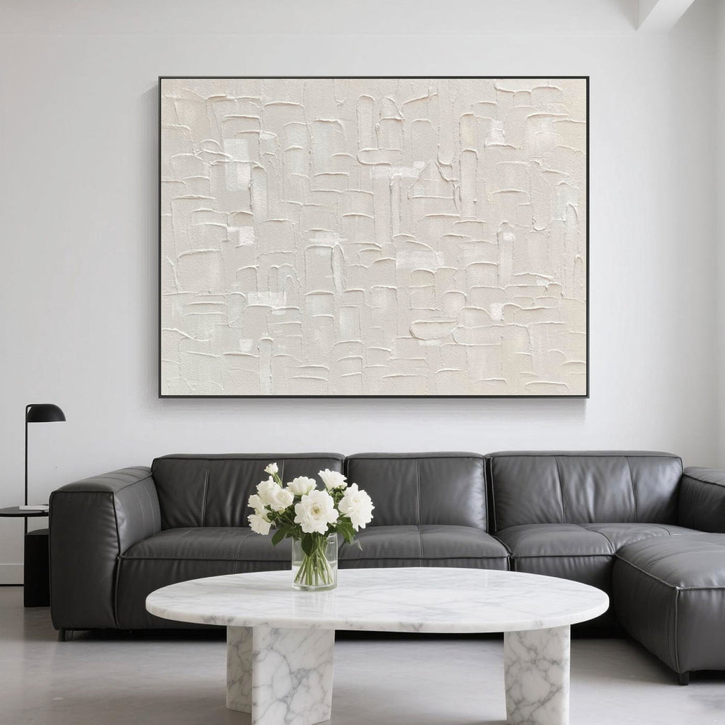 Beige art behind a gray sectional with marble furniture and floral accents.