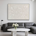 Beige art behind a gray sectional with marble furniture and floral accents.