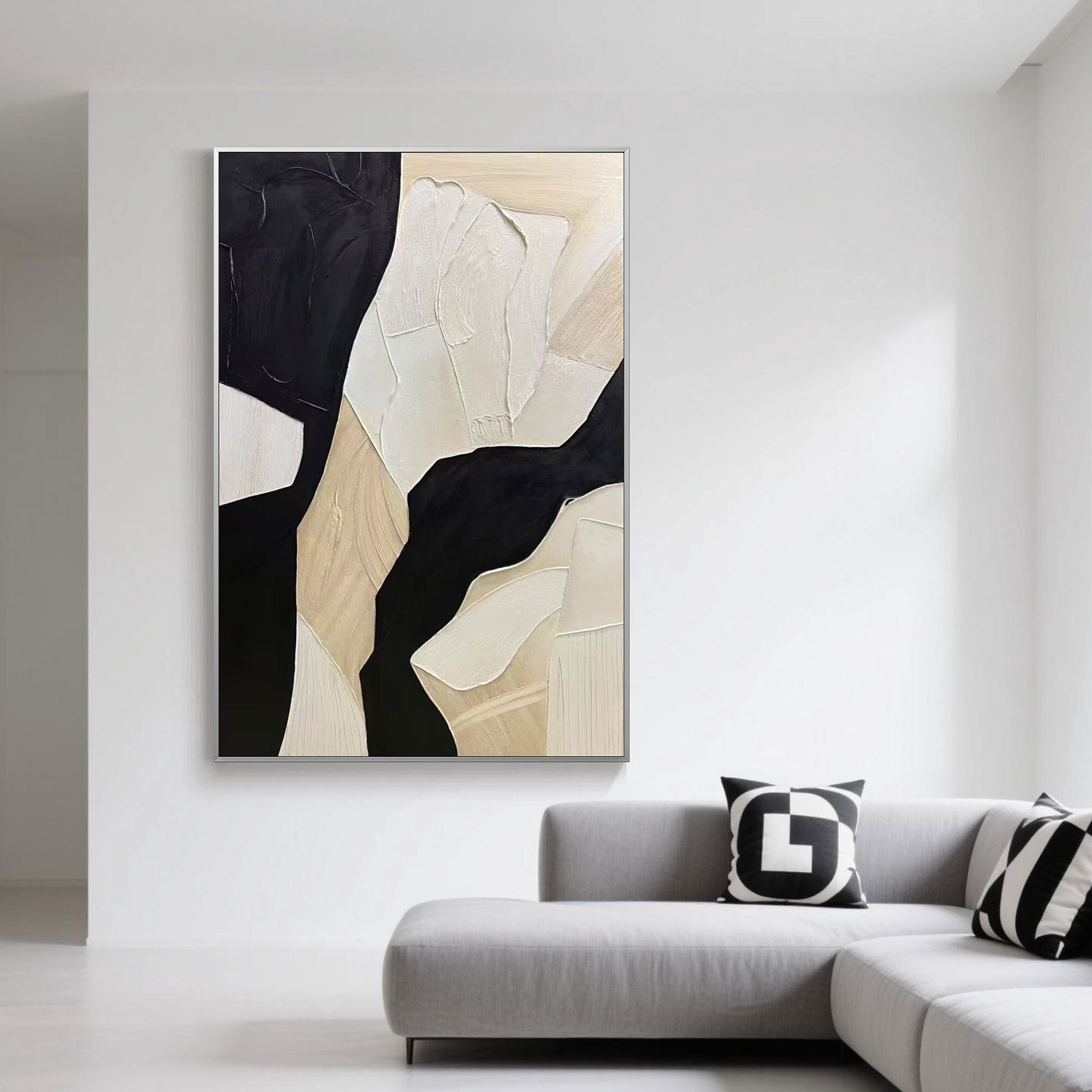 Vertical abstract geometric wall art in beige and black hangs above a minimalist grey sofa in a bright modern living room.