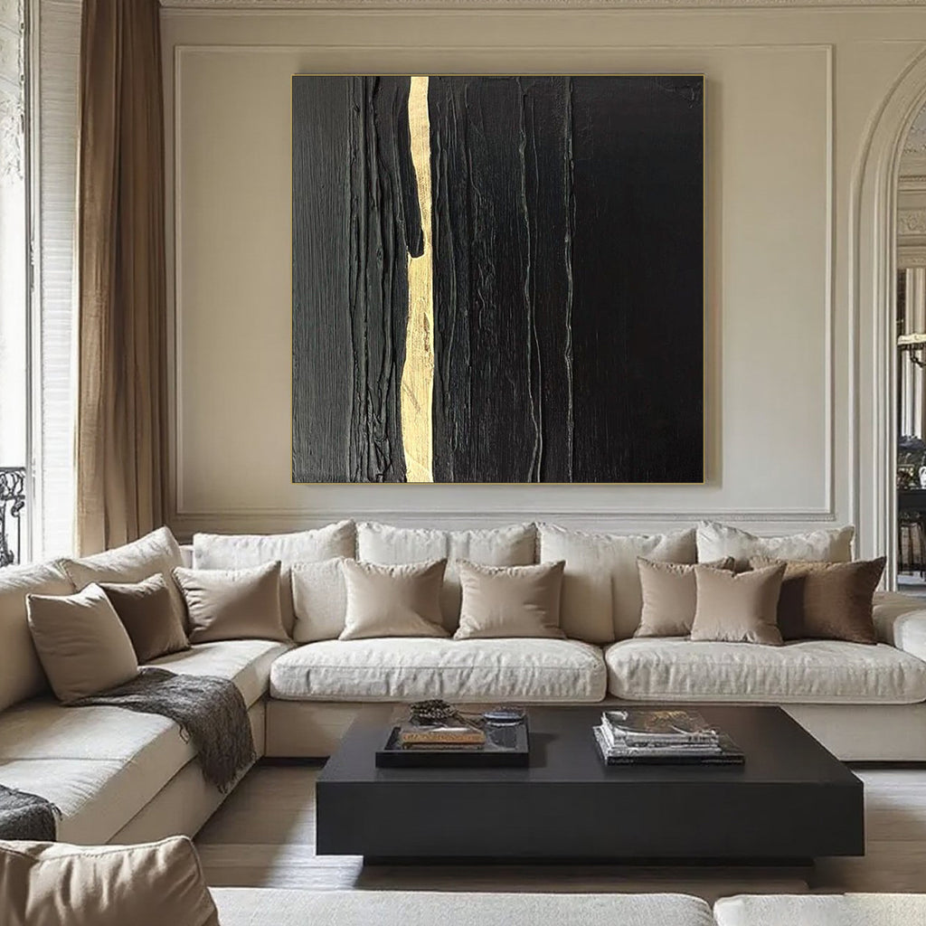 Abstract minimalist square canvas art with black and gold textured vertical strokes, titled Auric Rift, displayed on a wall in a contemporary living room.