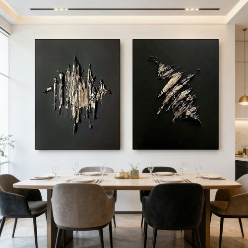 Two large 3D textured black and gold abstract wall art pieces, 'Fracture' and 'Flame', displayed in a modern dining room with a marble table and neutral chairs.
